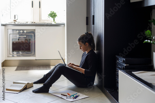 Adolescente coni capelli scuri raccolti e un maglia nera fa i compiti a casa seduta per terra photo