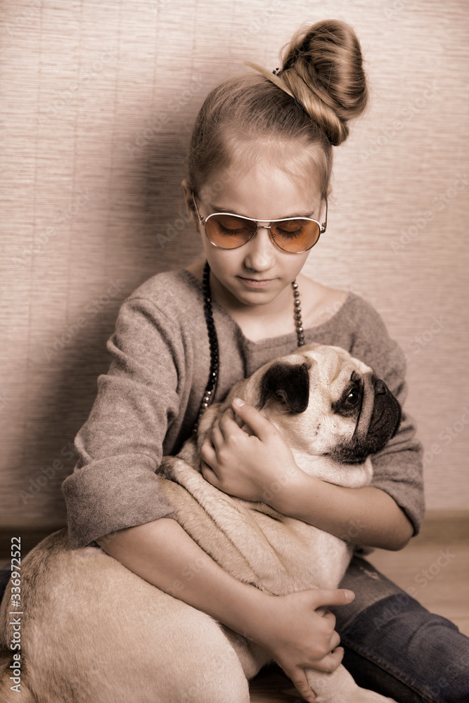Girl hugs a pug dog. There are sunglasses on the girl. The age of the girl is 9 years.