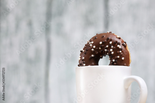 White coffee cup on a wooden table with chocolate and white chocolate donuts . Morning espresso. Morning cappuccino mug. 