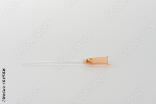 Part of orange intravenous cannula 14 G on white background, external diameter 2,1 mm, used in trauma, blood transfusion, surgery, ascites puncture.