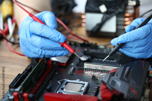 Close-up of middle-aged man measuring electrical voltage. Technician male repairing computer mainboard using digital multimeter. Technology and diy concept