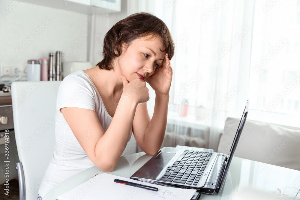 A young girl looks at a laptop in the kitchen in her apartment.