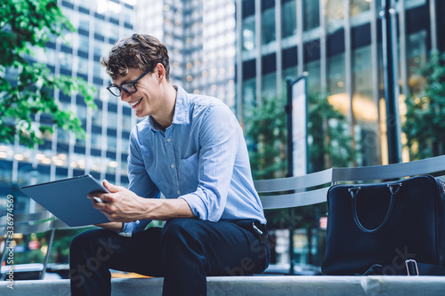 Cheerful man browsing tablet sitting on bench