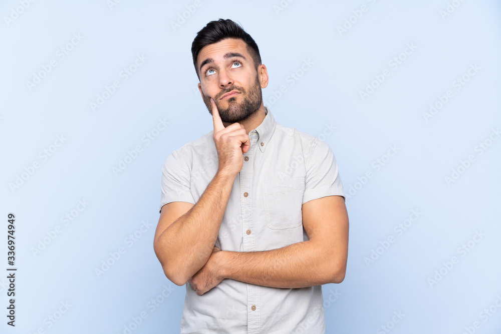 Young handsome man with beard over isolated blue background thinking an idea