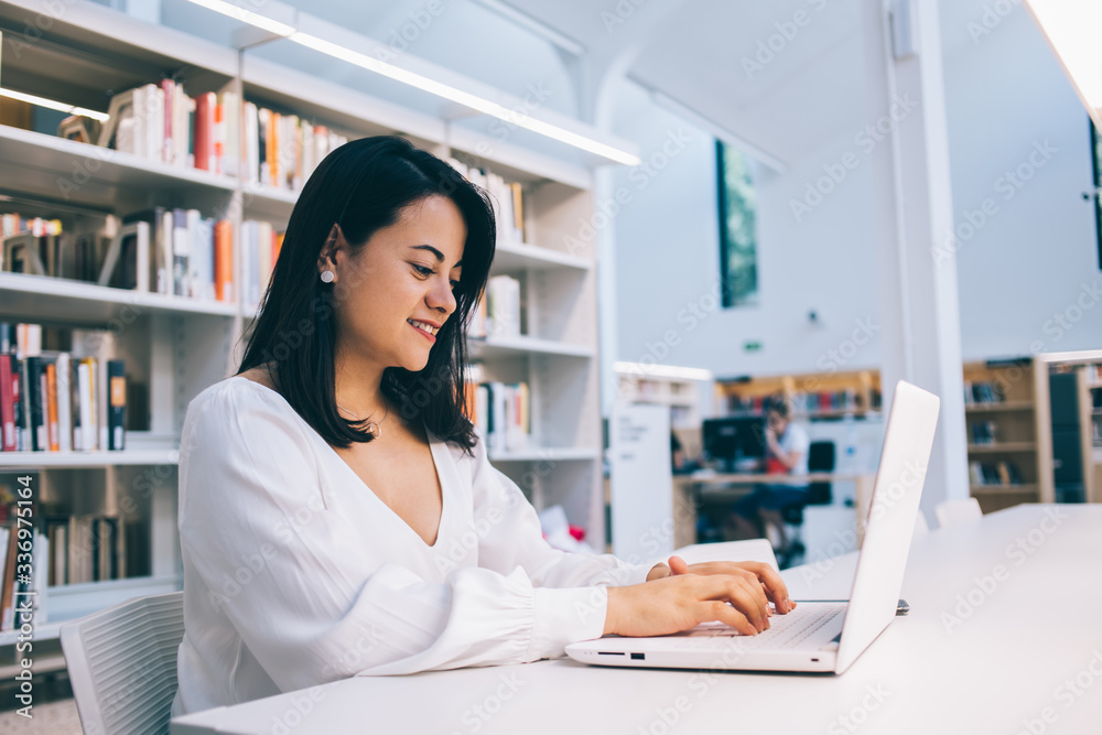 Young ethnic female sitting at table with laptop in library Young ethnic female sitting at table with laptop in library
