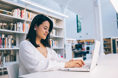 Young ethnic female sitting at table with laptop in library