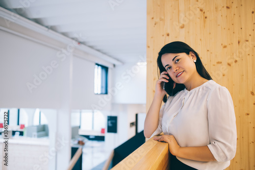 Cheerful female worker talking on mobile phone in office