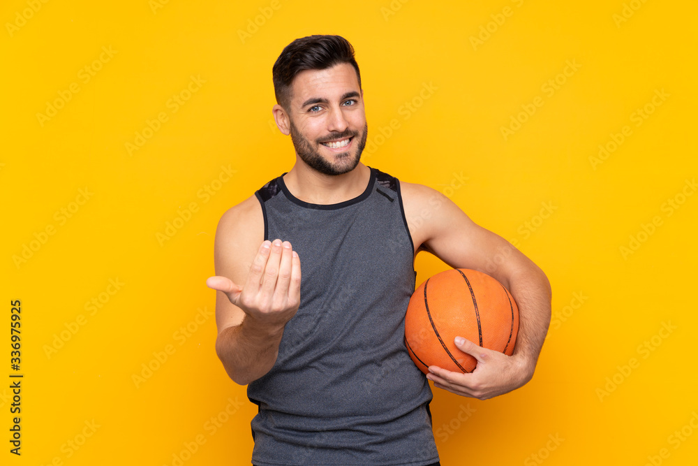 Handsome young basketball player man over isolated white wall inviting to come with hand. Happy that you came