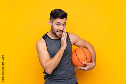 Handsome young basketball player man over isolated white wall whispering something