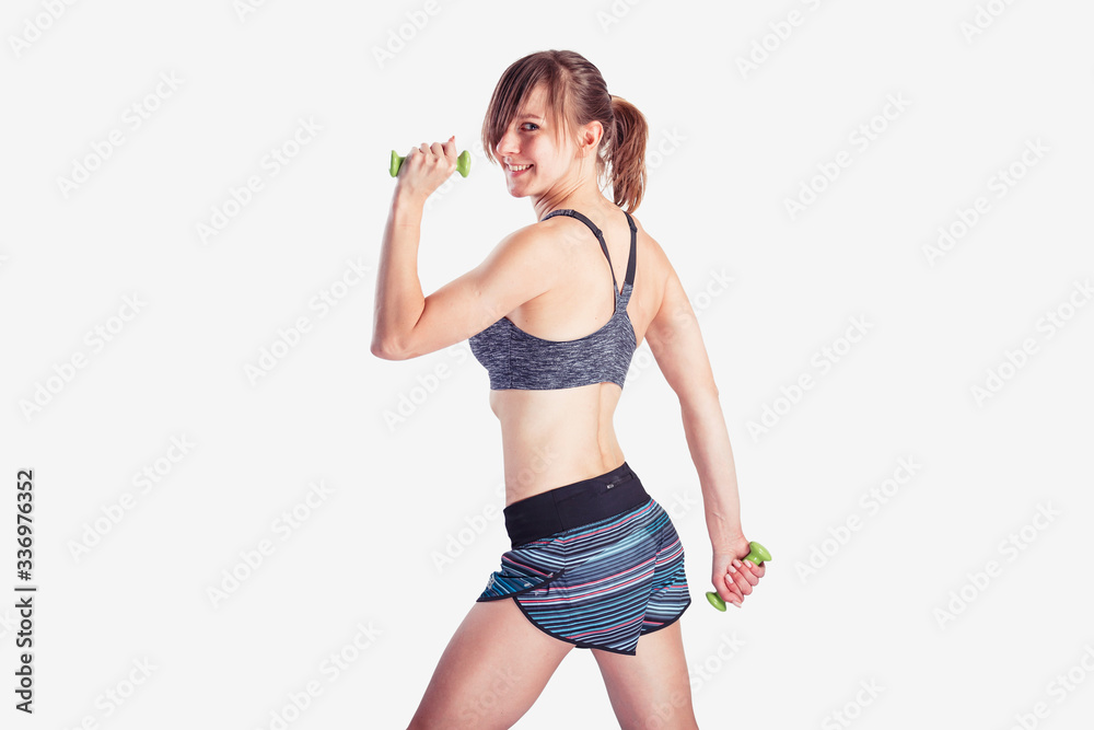 Sporty woman does the exercises with dumbbells on gray background. Photo of muscular woman in sportswear at studio Sporty woman does the exercises with dumbbells on gray background. Photo of muscular woman in sportswear at studio