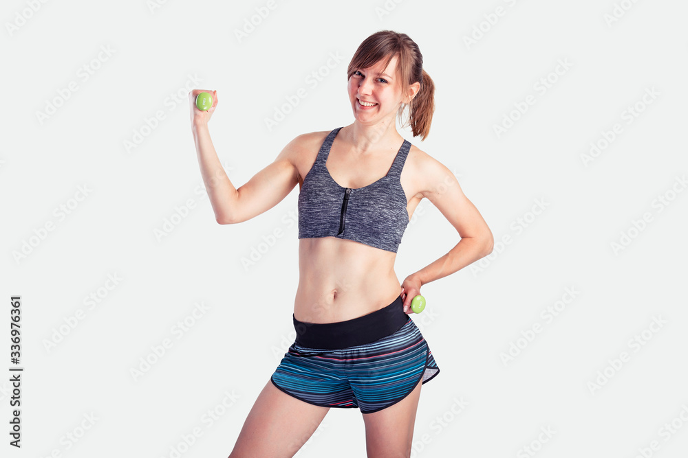 Sporty woman does the exercises with dumbbells on gray background. Photo of muscular woman in sportswear at studio Sporty woman does the exercises with dumbbells on gray background. Photo of muscular woman in sportswear at studio