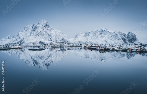 Scenic panorama of snow covered mountain range reflected in cold waters of arctic sea