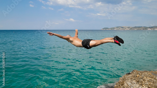 Mężczyzna skaczący do morza ze skał, uchwycony w locie.