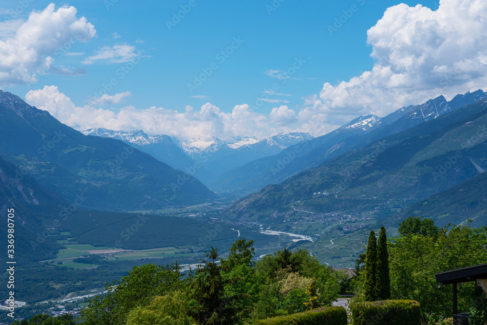 Mountain valley landscape. Beautiful view of Swiss mountains. Hazy blue mountains covered by fog. Alpine houses, meadows on the slopes and snow-capped mountains.