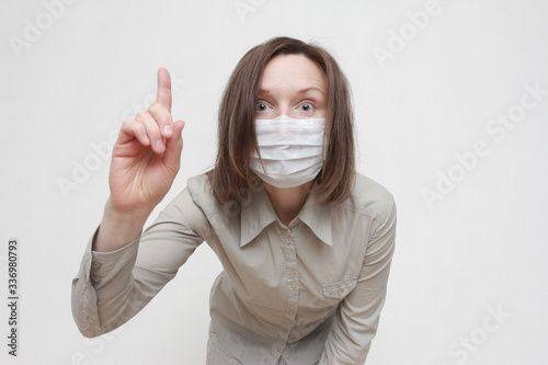 Anxious serious woman wearing medical raising index finger isolated over white background. Coronavirus, pandemic, protection, emotion, gesture