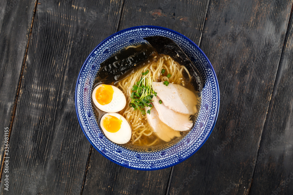 Top view on appetizing asian japanese shio ramen noodle soup with pickled agitama egg and chicken breast in a traditional blue bowl on the dark wooden table, horizontal