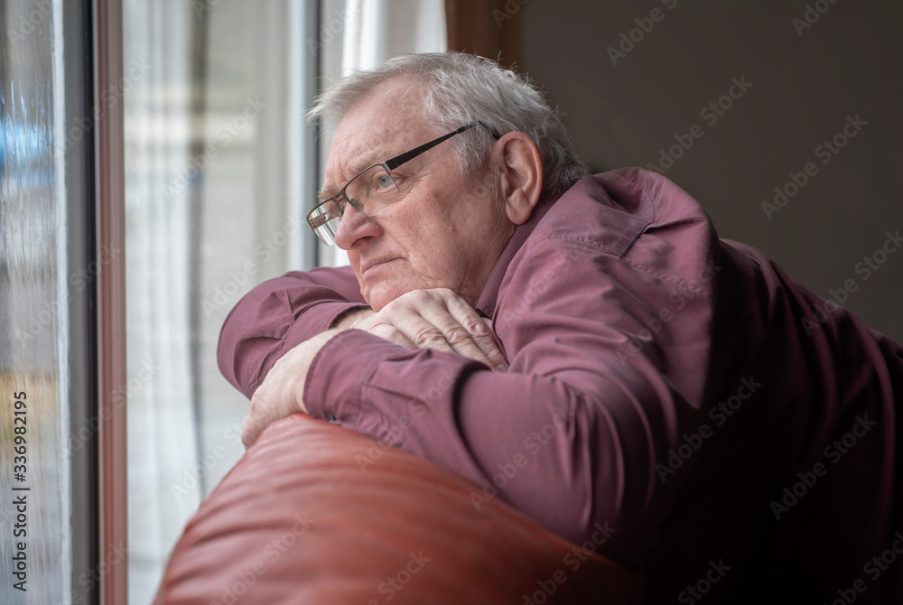 Bored man in sixties looking out the window in home Bored man in sixties looking out the window in home