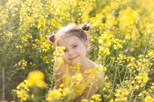 Cute girl in a yellow dress having fun in the field of flowering rape