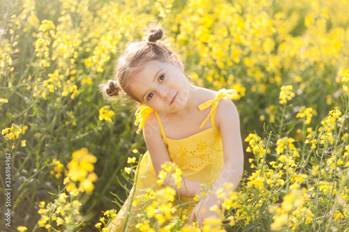 Cute girl in a yellow dress having fun in the field of flowering rape © Olga Gorchichko