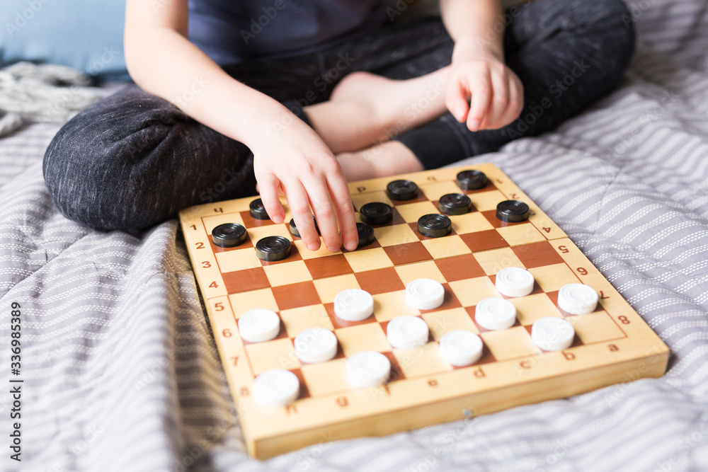 Young kid hands playing checkers table game on bed. Stay at home Quarantine concept. Board game and kids leisure concept. Family time. Young kid hands playing checkers table game on bed. Stay at home Quarantine concept. Board game and kids leisure concept. Family time.