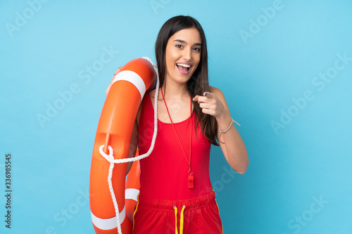 Lifeguard woman over isolated blue background with lifeguard equipment and surprised expression while pointing front