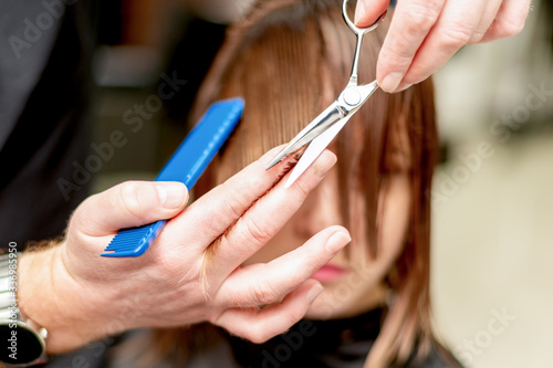 Hands of hairdresser cutting hair tips of woman in beauty salon.
