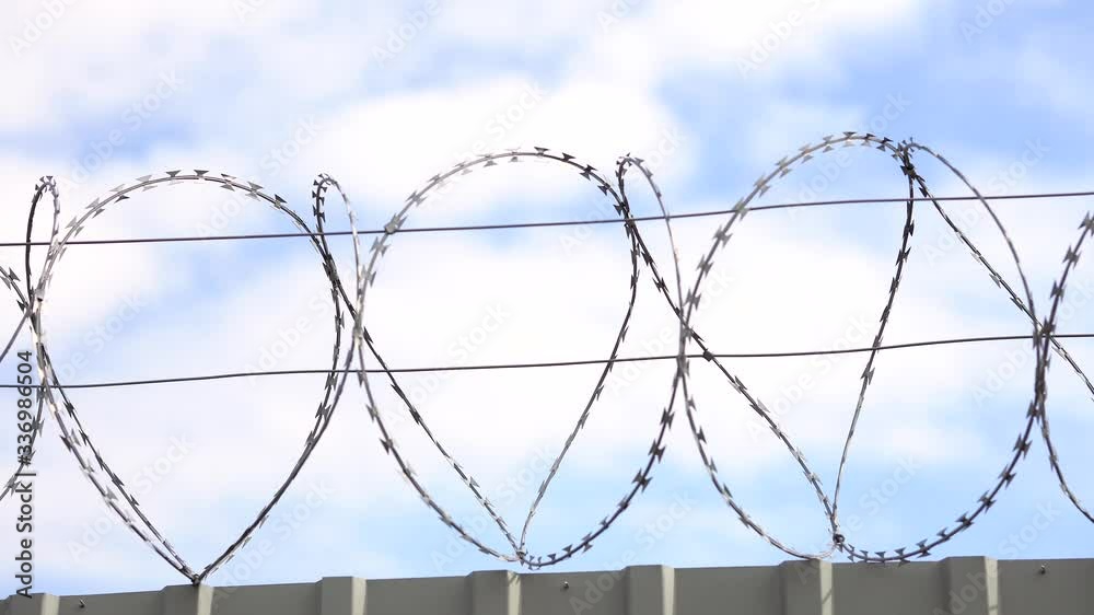 Barbed wire, razor wire on top of steel fence on blue sky background. Forbidden territory or protected area, military facility, prison or secret territory. Barbed wire, razor wire on top of steel fence on blue sky background. Forbidden territory or protected area, military facility, prison or secret territory.