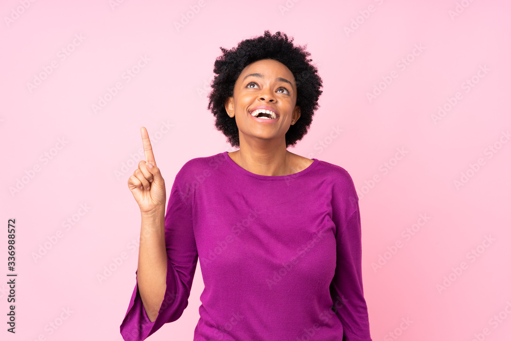 African american woman over isolated pink background pointing up and surprised