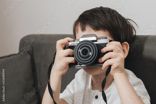 Beautiful smiling child (kid, boy) - photographer holding a instant camera intdoors