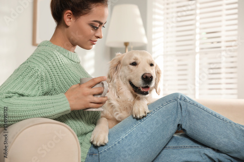 Young woman with cup of drink and her Golden Retriever on sofa at home. Adorable pet