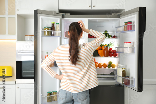 Fotografía Young woman near open refrigerator in kitchen, back view