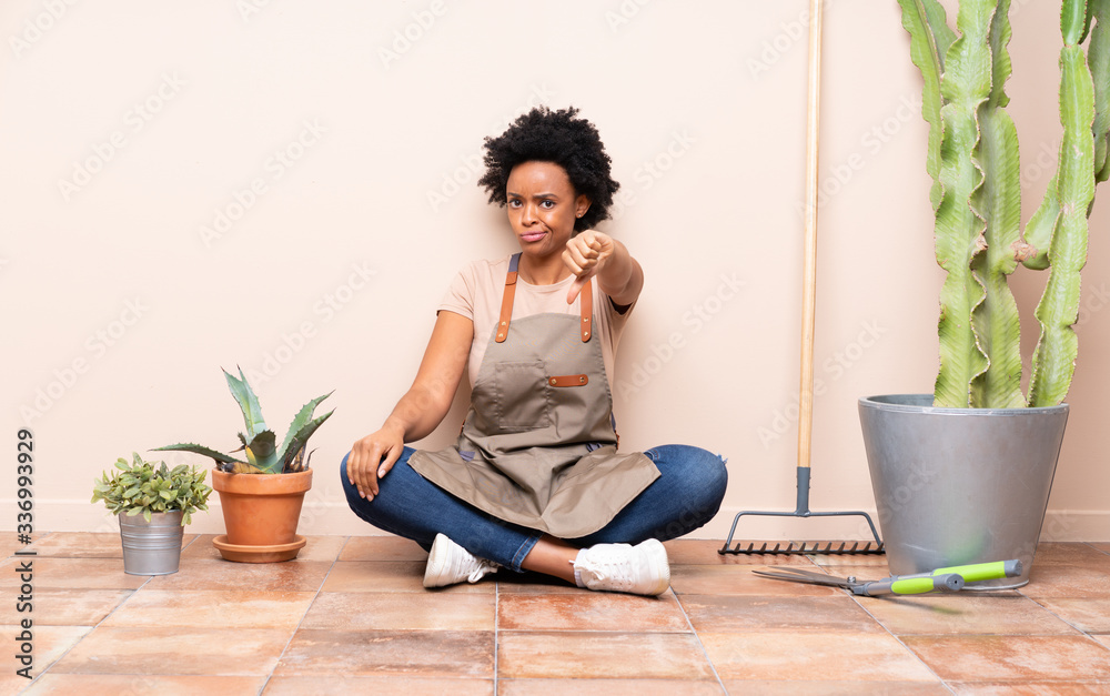 Gardener woman sitting on the floor showing thumb down with negative expression Gardener woman sitting on the floor showing thumb down with negative expression