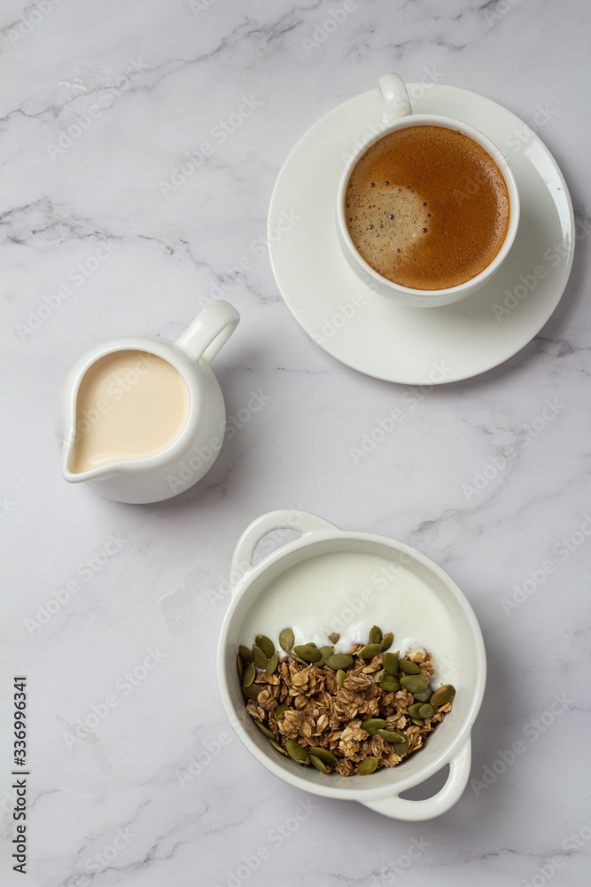 granola with seeds and yogurt in a white cup and black coffee with milk top view
granola with seeds and yogurt in a white cup and black coffee with milk top view