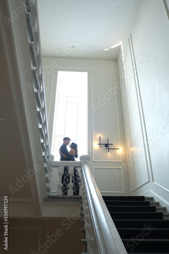 Young beautiful couple - a girl and a guy are standing or sitting on a white staircase inside a large beautiful building. 