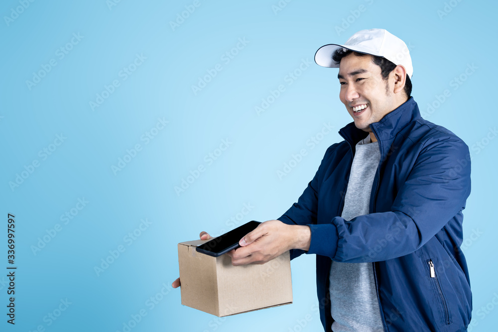 Delivery man is holding brown box parcel and smart phone for signs on blue background. Delivery man is holding brown box parcel and smart phone for signs on blue background.