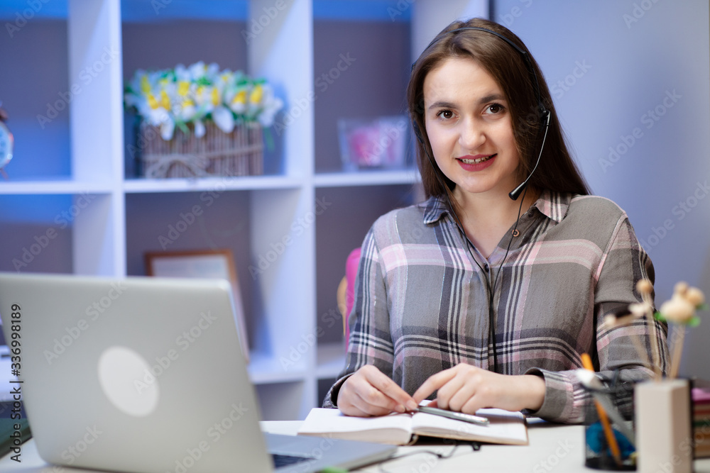 Positive charming woman working at home. Smiling young woman student wear headset using laptop for e learning course online teaching in internet at home Positive charming woman working at home. Smiling young woman student wear headset using laptop for e learning course online teaching in internet at home