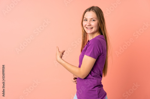 Teenager Ukrainian girl isolated on pink background pointing back