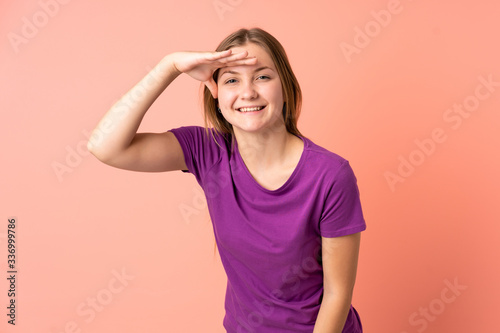 Teenager Ukrainian girl isolated on pink background looking far away with hand to look something