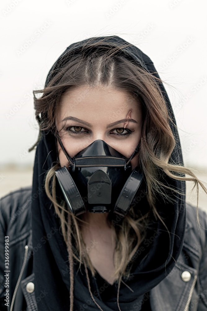 Portrait of a young woman wearing a black respirator, posing outdoors