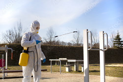 Kobieta w odzieży ochronnej dezynfekuje sprzęt sportowy na boisku
