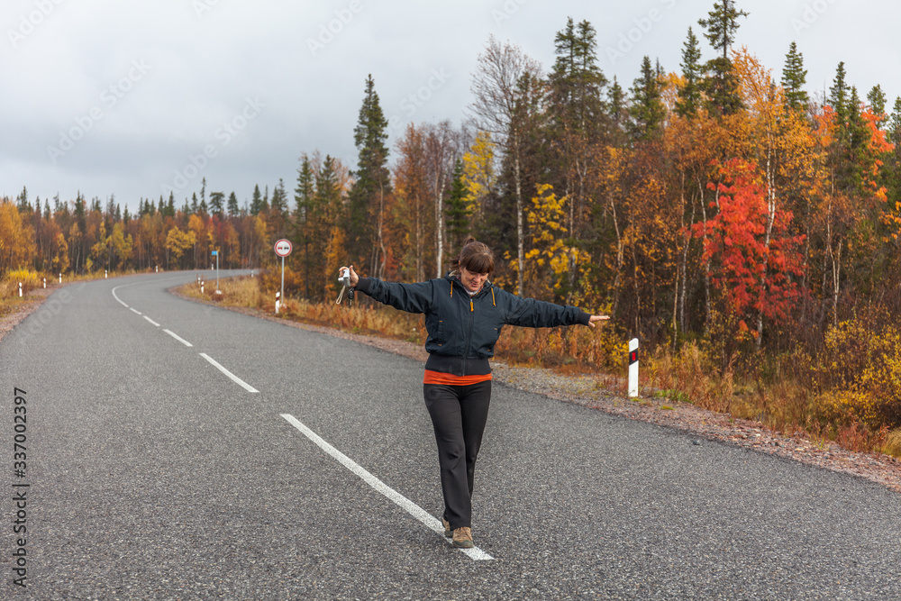 A middle-aged woman standing in the middle of the road with beautiful autumn forest, travel concept A middle-aged woman standing in the middle of the road with beautiful autumn forest, travel concept