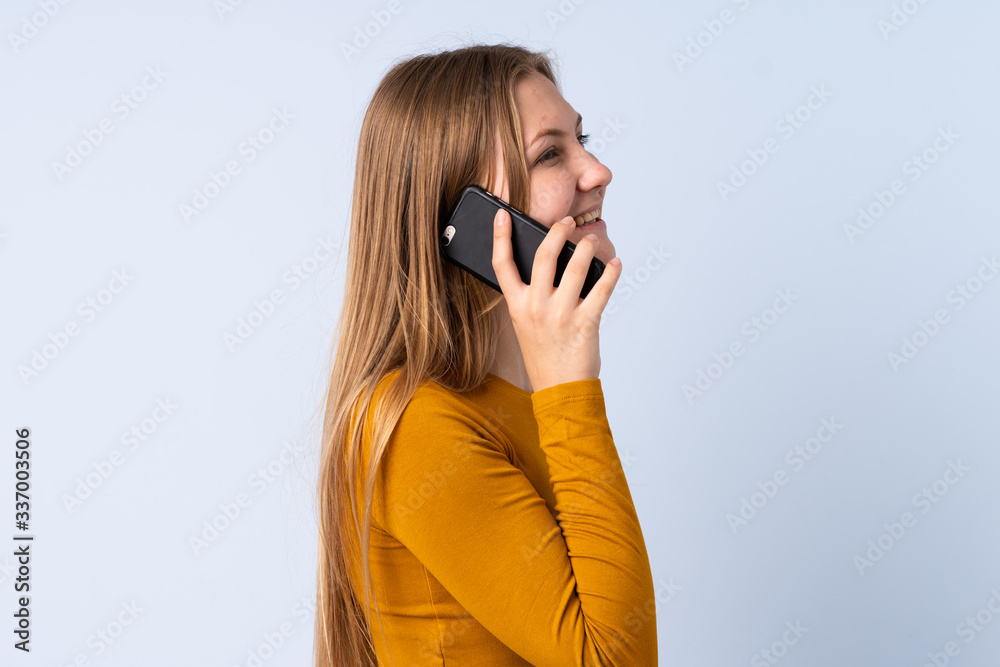 Teenager Ukrainian girl isolated on blue background keeping a conversation with the mobile phone with someone
