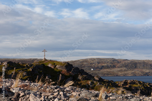 Russia, Arctic, Kola Peninsula, Teriberka: view with orthodox wooden cross on rocky hill and calm Barents Sea near center of the old Russian settlement small fishing village - travel religion.