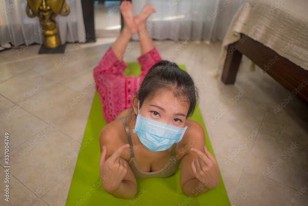 yoga against covid-19 lockdown quarantine stress - young beautiful and happy Asian Korean woman in protective mask doing yoga workout at home bedroom