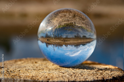 Inverted image of the river and its banks in a glass ball standing on a stump. Selective focus.