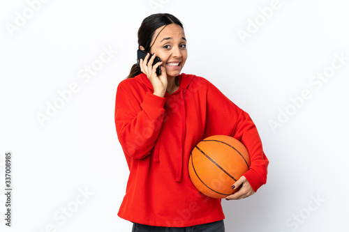 Young woman playing basketball over isolated white background keeping a conversation with the mobile phone with someone © luismolinero