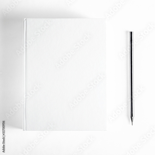 Mockup of closed blank square book and black pencil at white textured paper background © Nataliia