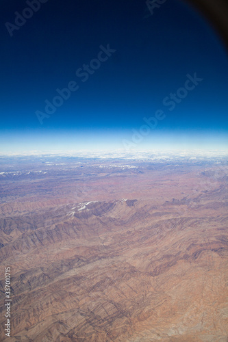 Mountains with snowy peaks from the window of an airplane on a sunny day.