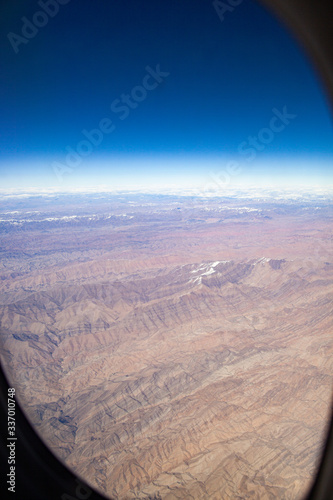 Mountains with snowy peaks from the window of an airplane on a sunny day.