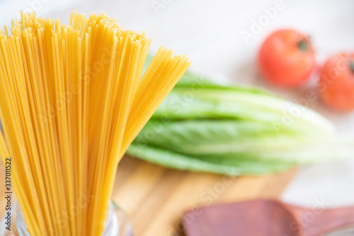 Raw Italian spaghetti in the glass jar and ingredients for cooking.